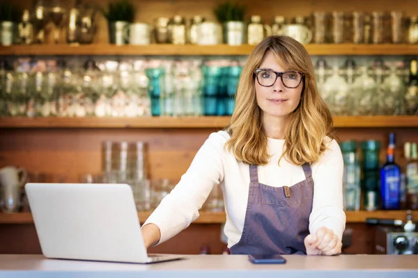 自信成熟的小咖啡馆店主女商人站在柜台后面 一边工作一边用笔记本电脑 — 图库照片