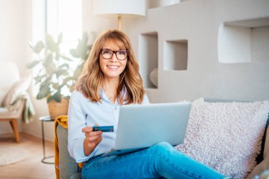 Elinde banka kartı olan bir kadının evde online ödeme yaparken dizüstü bilgisayar kullanması..