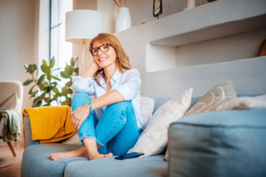 Mutlu, olgun bir kadının evde kanepede dinlenip düşünceli bir şekilde baktığı uzun bir çekim..