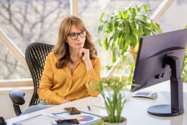 Kendine güvenen bir iş kadını, bilgisayarının başında oturup çalışırken düşünceli görünüyor. Merkez Ofis.