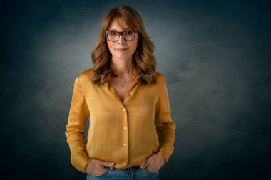 İzole edilmiş karanlık arka planda duran orta yaşlı çekici kadının stüdyo portresi. Boşluğu kopyala.