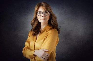 Stüdyo portresi, kolları bağlı, karanlık arka planda duran orta yaşlı çekici bir kadın. Boşluğu kopyala.