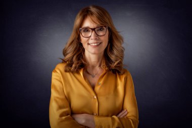 Stüdyo portresi, kolları bağlı, karanlık arka planda duran orta yaşlı çekici bir kadın. Boşluğu kopyala.