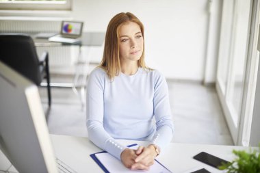 High angle shot of thinking young businesswoman sitting at office desk and looking away while working. 
