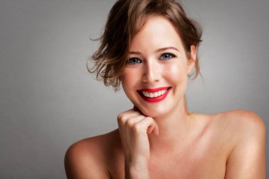 Fotokopi alanı ile izole edilmiş gri arka planda poz verirken mükemmel ciltli, kırmızı ruj süren muhteşem genç bir kadının portresi. Eller çenede.. 