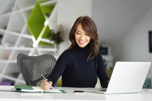 一位自信的中年女商人 穿着高领毛衣 坐在笔记本电脑后面的写字台前 为新项目工作 — 图库照片