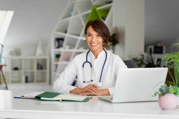 Trabalhadora Saúde Sorrindo Fazendo Alguma Papelada Usando Laptop Enquanto Trabalhava — Fotografia de Stock