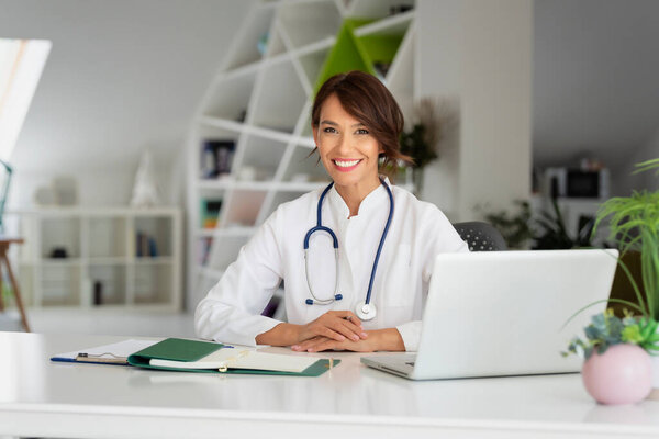 Smiling female healthcare worker doing some paperwork and using laptop while working at doctor's office