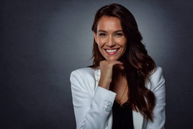 Çekici, orta yaşlı, dişlek, ceketli, koyu gri arka planda duran bir kadının stüdyo portresi. Boşluğu kopyala. 