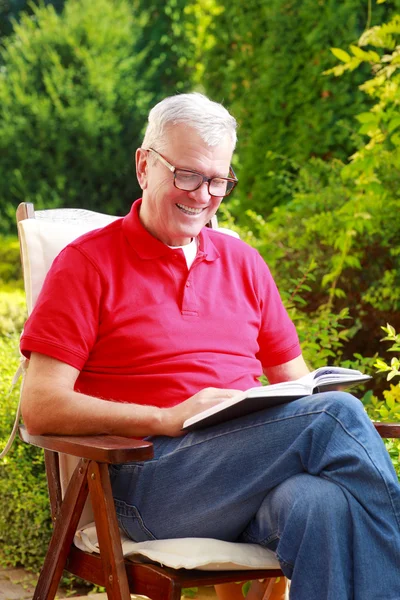 Senior man in tuin leesboek — Stockfoto