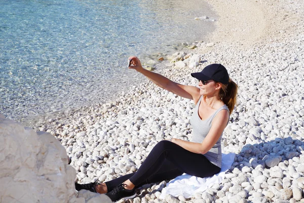 Fit woman sitting at pebble beach — Stock Photo, Image