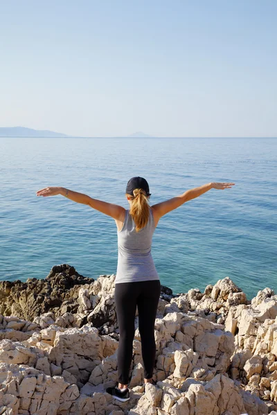 Fit woman with arms raised by sea — Stock Photo, Image