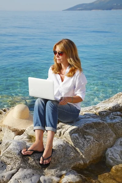 Vrouw met laptop zitting door de zee — Stockfoto