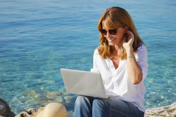 Γυναίκα με φορητό υπολογιστή που κάθεται δίπλα στη θάλασσα — Φωτογραφία Αρχείου