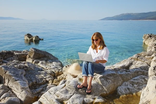 Donna con computer portatile seduta vicino al mare — Foto Stock