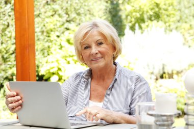 Evde dizüstü bilgisayarı olan yaşlı bir kadın.