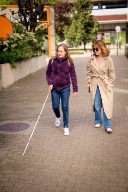 Görme engelli ve işitme engelli bir kadın, kız arkadaşıyla şehirde yürüyor. Görme engelli bir kadın elinde beyaz bir baston tutuyor ve konuşuyor. Tam uzunluk. 