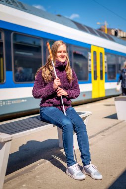 Tren istasyonunda dikilip demiryolunu bekleyen beyaz bastonlu kör kadının portresi. Treni bekleyen görme engelli bir kadın. Günlük kıyafetler. Tam uzunluk. 