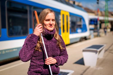 Tren istasyonunda dikilip demiryolunu bekleyen beyaz bastonlu kör kadının portresi. Treni bekleyen görme engelli bir kadın. Günlük kıyafetler. Tam uzunluk. 