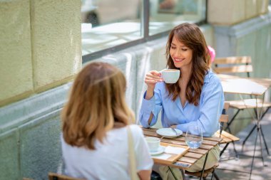 Kafede oturup sohbet eden iki güzel kadın. Kahve içip dedikodu yapan iki bayan arkadaş. Orta yaşlı kadınlar günlük kıyafetler giyerler.. 