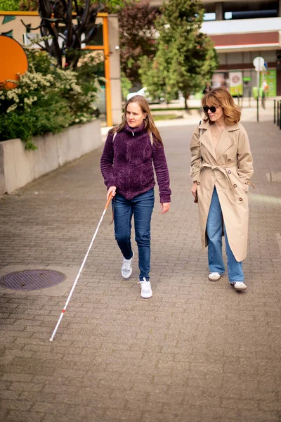 Görme engelli ve işitme engelli bir kadın, kız arkadaşıyla şehirde yürüyor. Görme engelli bir kadın elinde beyaz bir baston tutuyor ve konuşuyor. Tam uzunluk. 