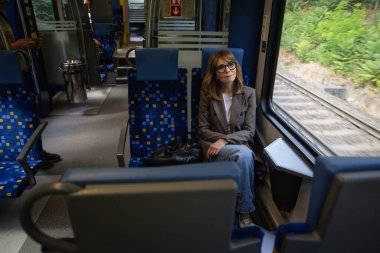 Sarı saçlı kadın trende oturuyor ve düşünceli görünüyor. Kendine güvenen bir kadın şık giyiniyor.. 