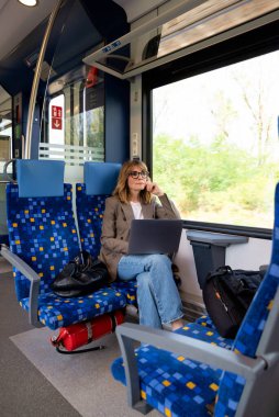 Trenle seyahat ederken dizüstü bilgisayarında çalışan sarışın kadın. Modern bir trende tek başına oturan kendinden emin bir kadın. Uzak çalışma.