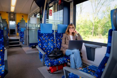 Trenle seyahat ederken dizüstü bilgisayarında çalışan sarışın kadın. Modern bir trende tek başına oturan kendinden emin bir kadın. Uzak çalışma.