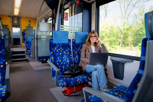 Trenle seyahat ederken dizüstü bilgisayarında çalışan sarışın kadın. Modern bir trende tek başına oturan kendinden emin bir kadın. Uzak çalışma.
