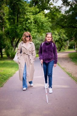 Görme engelli ve işitme engelli bir kadın, kız arkadaşıyla şehirde yürüyor. Görme engelli bir kadın elinde beyaz bir baston tutuyor ve konuşuyor. Tam uzunluk. 