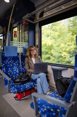 Trenle seyahat ederken dizüstü bilgisayarında çalışan sarışın kadın. Modern bir trende tek başına oturan kendinden emin bir kadın. Uzak çalışma.