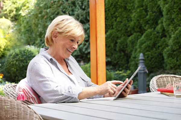 Äldre kvinna i trädgård med hjälp av Tablet PC — Stockfoto