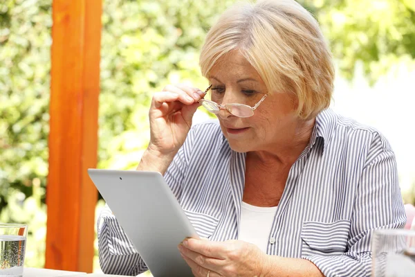 Äldre kvinna i trädgård med hjälp av Tablet PC — Stockfoto