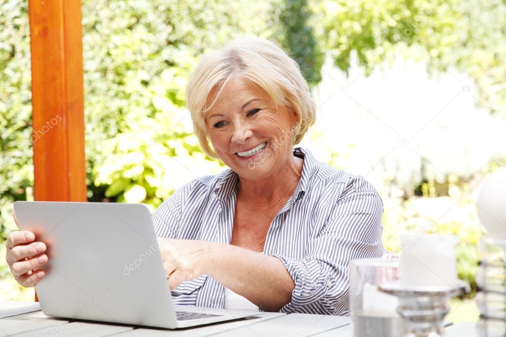 senior woman sitting at garden with laptop