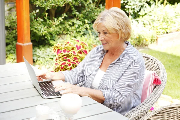 Donna anziana in giardino con il suo computer portatile — Foto Stock