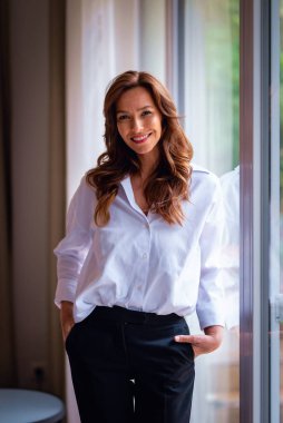 Modern oturma odasında pencereli gülümseyen kadın portresi. Çekici kadın, kumral saçlı, kameraya gülümseyen.. 