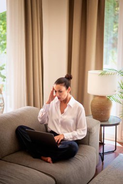 Kendinden emin orta yaşlı bir kadın evden uzakta çalışıyor. Dizüstü bilgisayar kullanırken şok oldum. Gündelik görünüş, rahat ve modern iç mekan. Merkez ofis. Serbest çalışma..