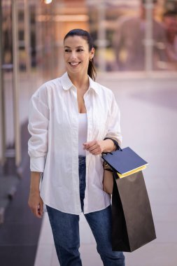 Alışveriş merkezinde yürüyen ve vitrinlere bakan orta yaşlı bir kadın. Sarı saçlı, sıradan kıyafetler giyen bir kadın..