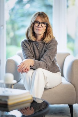 Çekici orta yaşlı kadın evdeki koltukta dinleniyor. Süveter ve pantolon giyen sarışın kadın. Tam boy çekim.