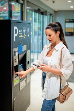 Güzel bir kadın akıllı telefonuyla park ediyor. Temassız ödeme. İş kadını park yeri için mobil ödeme yapıyor..