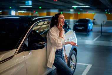 Arabasına yaslanıp telefonunu kullanan güzel bir kadın. Esmer, akıllı bir telefon tutan ve sıradan kıyafetler giyen bir kadın..