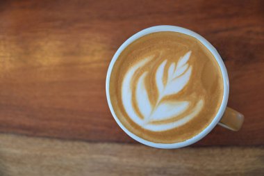 Sabah içmek için ahşap masadaki latte sanat kahvesinin en üst görüntüsü.