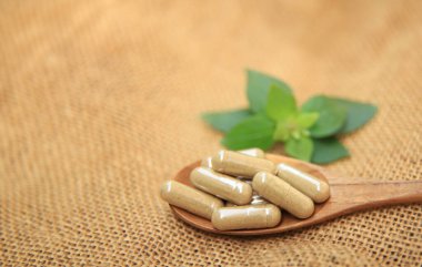 Sağlık hizmetleri için kapsüllerdeki sağlıklı gıda ilaçları kaşık üzerinde bitki yaprağı ile yenir.