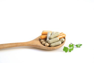 Kapsüllerdeki bitkisel ilaçlar tahta kaşık üzerinde sağlıklı yaşam tarzı ve sağlık sigortası konsepti için beyaz masa.