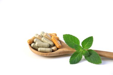 Kapsüllerdeki bitkisel ilaçlar tahta kaşık üzerinde sağlıklı yaşam tarzı ve sağlık sigortası konsepti için beyaz masa.