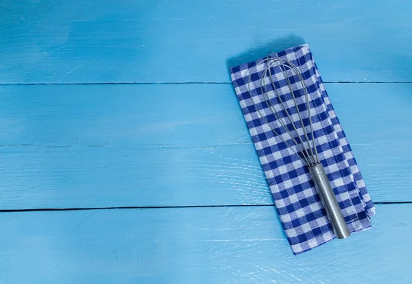 Whisk and tea towel on blue wooden background — Stock Photo, Image