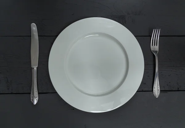 Cutlery and plate on a black wood background — Stok Foto