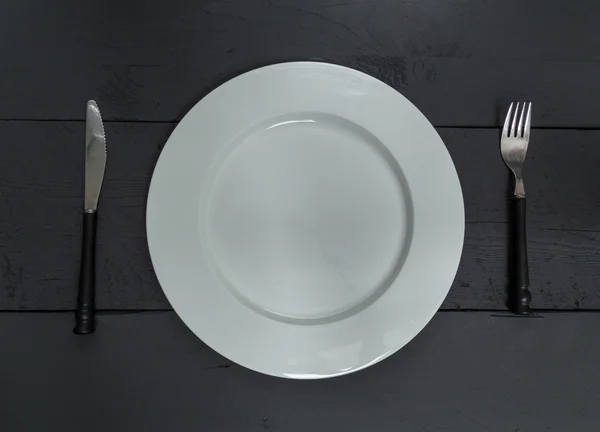 Cutlery and plate on a black wood background — Stok Foto