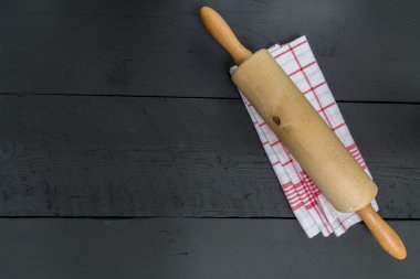 Rolling pin and dishcloth on black wooden background clipart