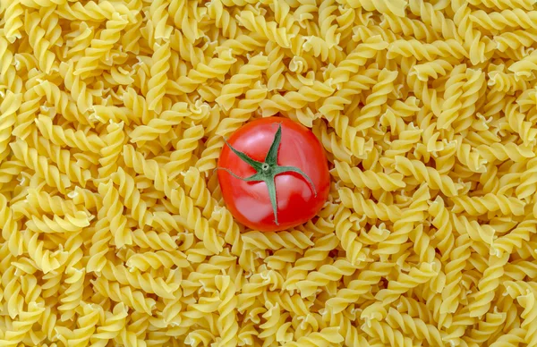 Tomato with fusilli pasta as background — Stock Photo, Image